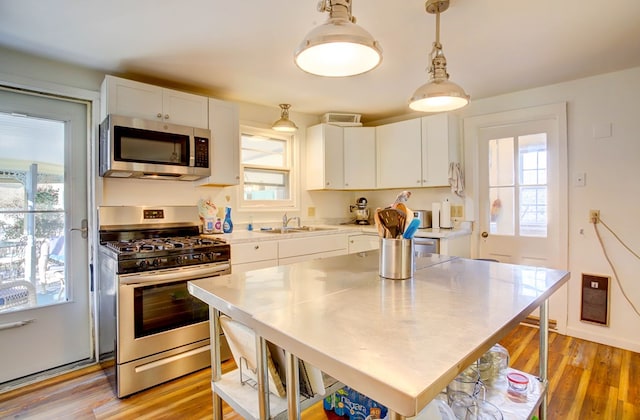 kitchen with stainless steel appliances, sink, decorative light fixtures, a center island, and white cabinetry