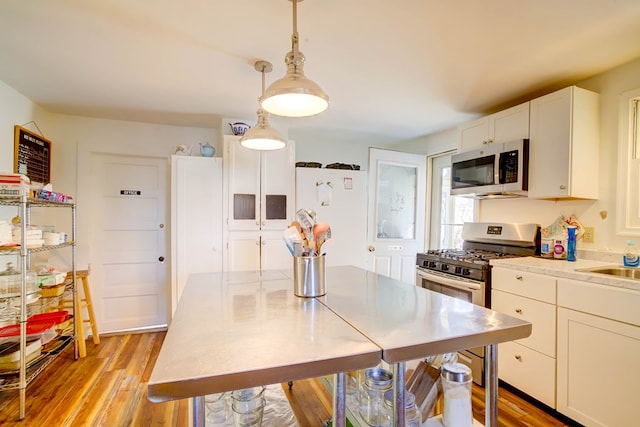 kitchen with white cabinetry, light hardwood / wood-style flooring, hanging light fixtures, and appliances with stainless steel finishes