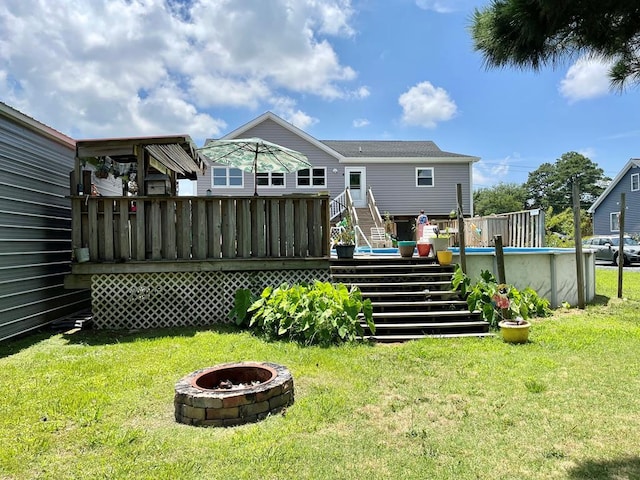 rear view of property featuring a fire pit, a pool side deck, and a lawn