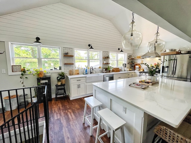 kitchen with appliances with stainless steel finishes, vaulted ceiling, sink, white cabinets, and hanging light fixtures