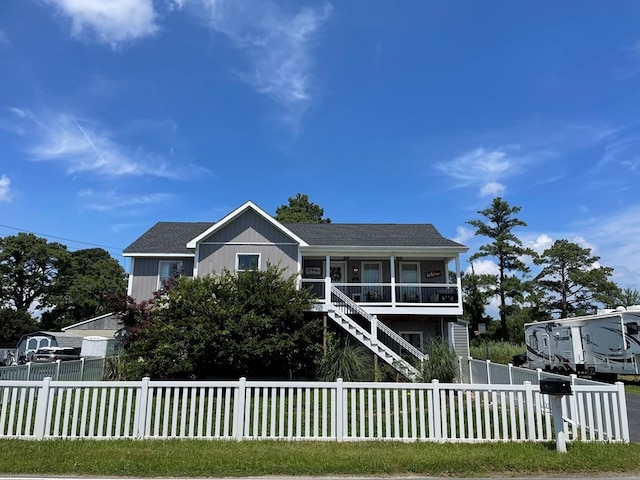 view of front of home featuring stairway, covered porch, a fenced front yard, and a shingled roof