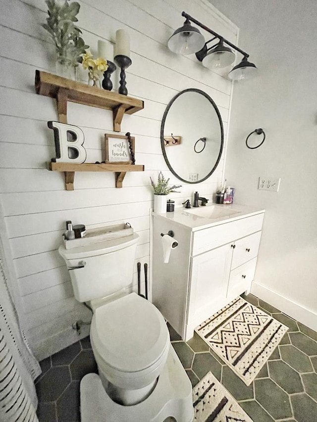 bathroom with baseboards, toilet, wood walls, and vanity