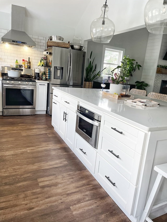 kitchen featuring white cabinetry, stainless steel appliances, wall chimney range hood, backsplash, and pendant lighting