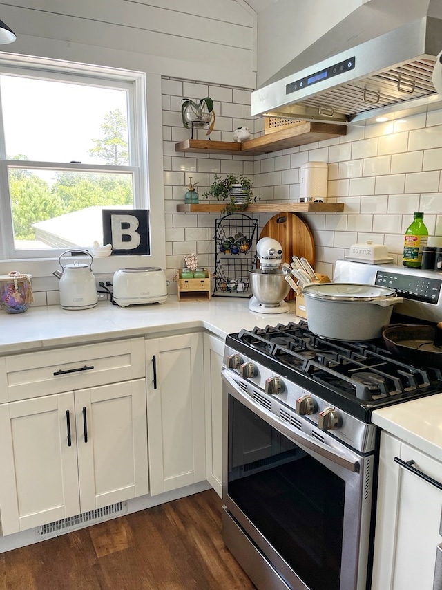 kitchen featuring tasteful backsplash, white cabinets, wall chimney range hood, and stainless steel gas range