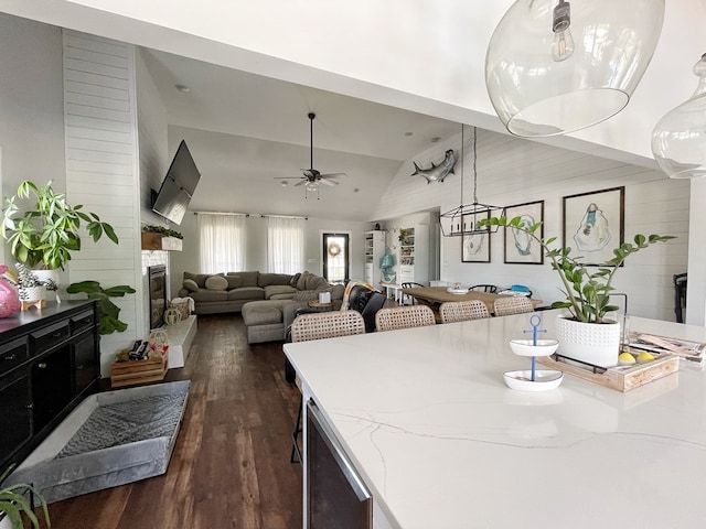 dining room featuring beverage cooler, ceiling fan, a stone fireplace, dark wood-type flooring, and vaulted ceiling