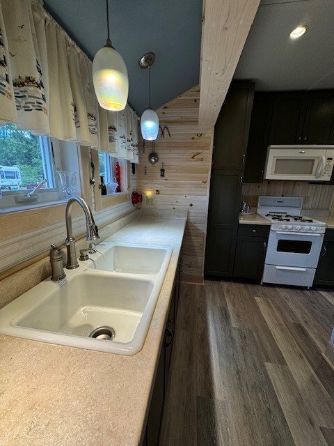 kitchen featuring white appliances, sink, decorative light fixtures, dark hardwood / wood-style floors, and wood walls