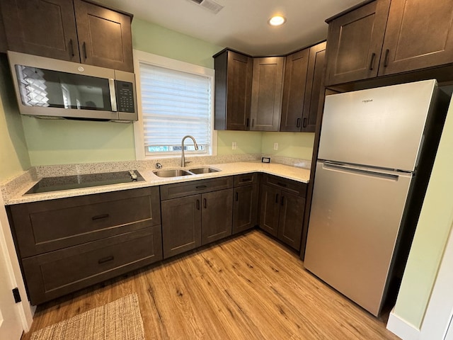 kitchen with sink, stainless steel appliances, dark brown cabinets, and light wood-type flooring