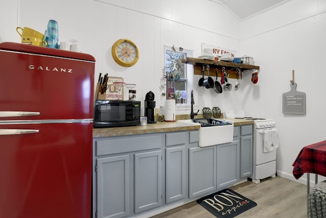 kitchen featuring light wood-type flooring, gray cabinetry, vaulted ceiling, white range with electric stovetop, and fridge