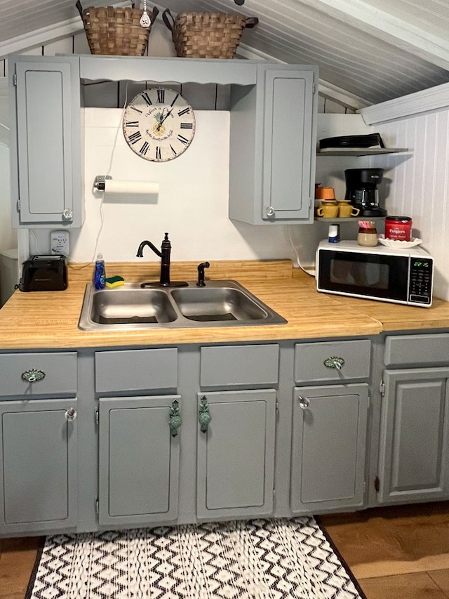 kitchen with gray cabinetry, sink, hardwood / wood-style floors, and vaulted ceiling