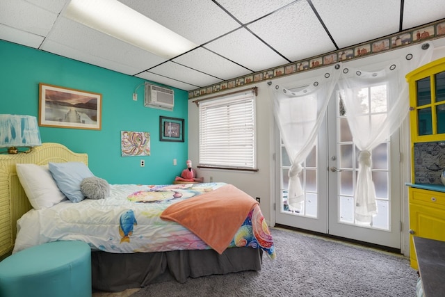 carpeted bedroom with a paneled ceiling, french doors, a wall mounted air conditioner, and access to exterior