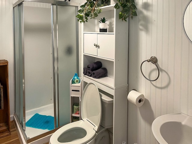 bathroom featuring an enclosed shower, toilet, hardwood / wood-style floors, and wooden walls