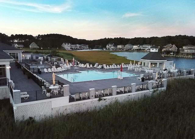 pool at dusk featuring a water view and a patio