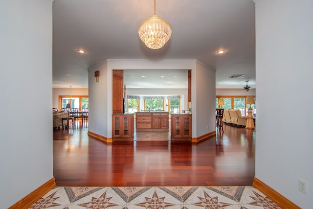 hallway featuring a chandelier, dark hardwood / wood-style floors, crown molding, and a healthy amount of sunlight