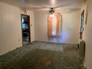 spare room featuring ceiling fan, wood walls, carpet floors, and heating unit