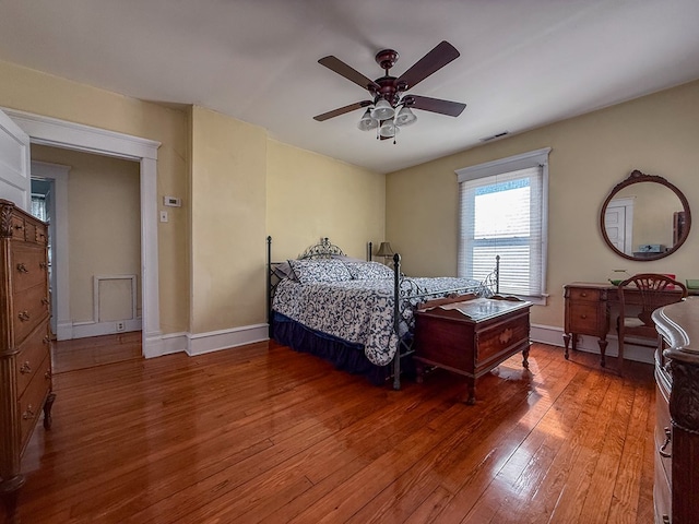 bedroom with a ceiling fan, wood finished floors, visible vents, and baseboards