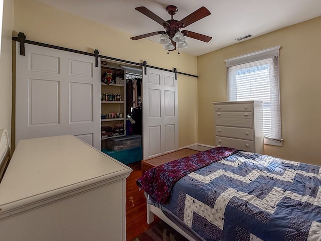 bedroom with a closet, visible vents, a barn door, ceiling fan, and wood finished floors