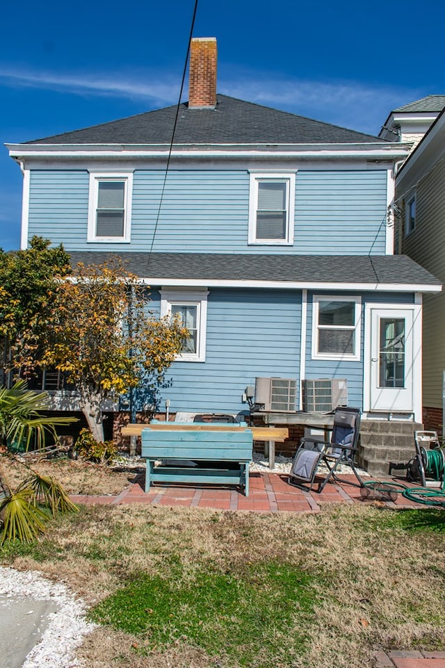 back of property with a patio area, a shingled roof, a chimney, and a yard