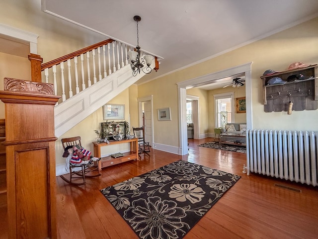 entryway featuring wood finished floors, baseboards, stairs, radiator heating unit, and crown molding