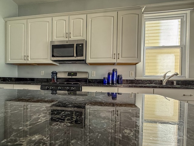 kitchen with white cabinets, dark stone counters, stainless steel appliances, and a sink