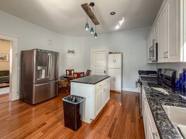 kitchen featuring white cabinets, dark stone counters, wood finished floors, a center island, and stainless steel appliances