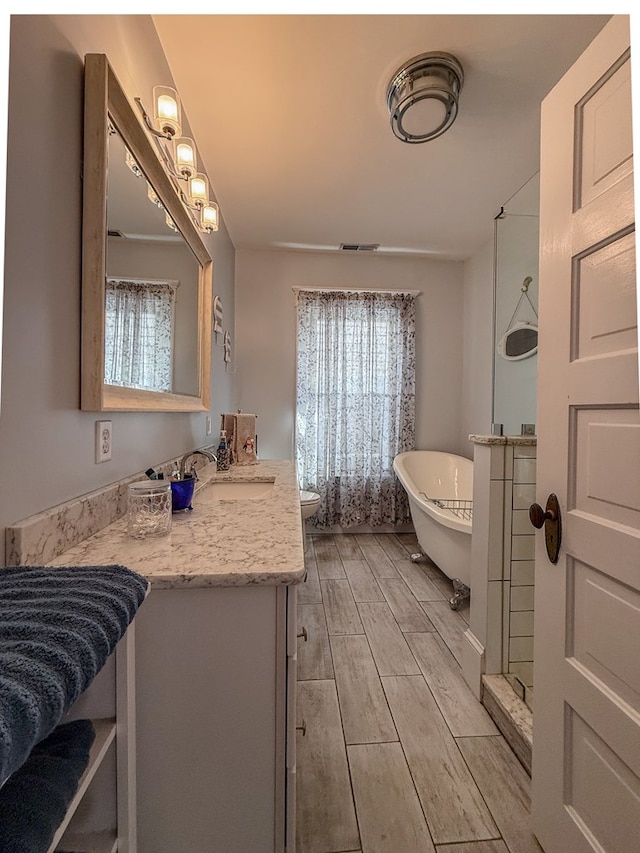 bathroom featuring toilet, wood tiled floor, a freestanding bath, vanity, and a healthy amount of sunlight