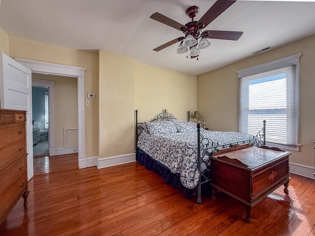 bedroom with ceiling fan, wood finished floors, visible vents, and baseboards