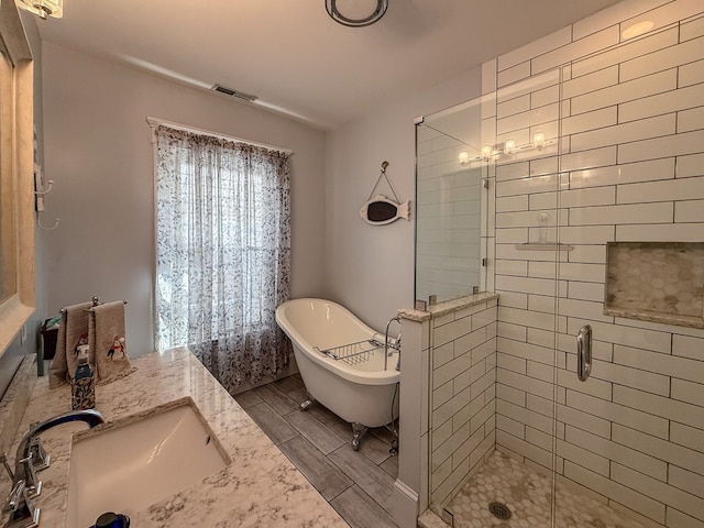 bathroom featuring wood finish floors, vanity, visible vents, a soaking tub, and a stall shower