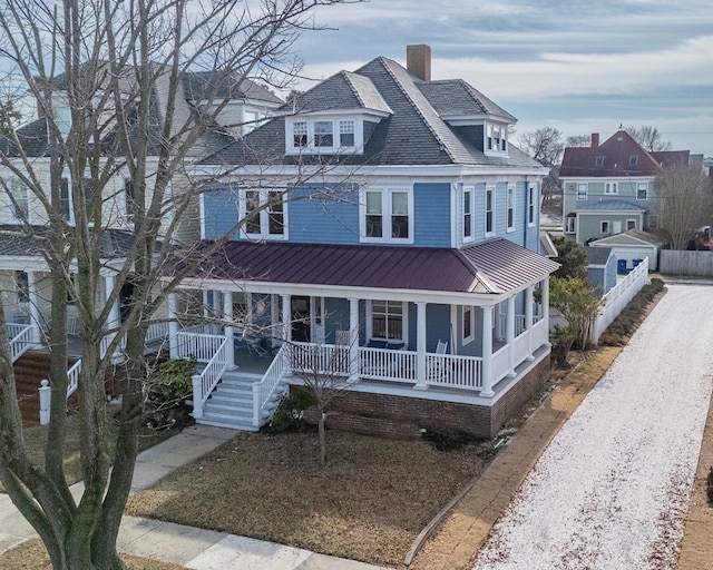 traditional style home featuring gravel driveway, a chimney, covered porch, a standing seam roof, and metal roof