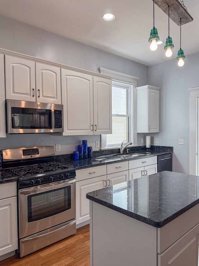 kitchen featuring a center island, decorative light fixtures, light wood finished floors, appliances with stainless steel finishes, and white cabinets