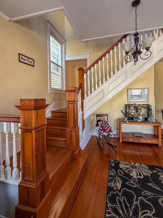 stairway featuring an inviting chandelier, wood-type flooring, ornamental molding, and baseboards