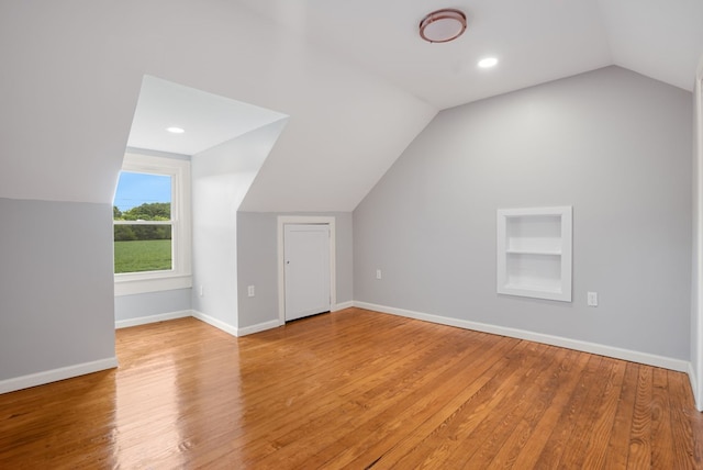 bonus room featuring built in shelves, light wood-type flooring, and lofted ceiling