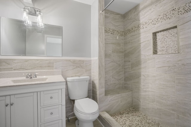 bathroom featuring tiled shower, vanity, tile walls, and toilet