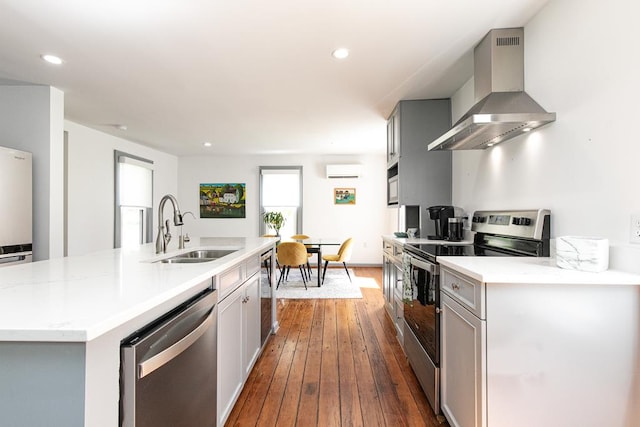 kitchen with wall chimney range hood, sink, gray cabinets, appliances with stainless steel finishes, and a wall mounted AC