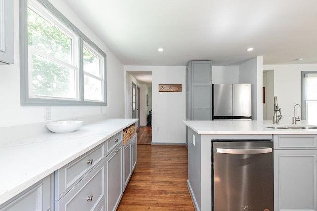 kitchen featuring sink, hardwood / wood-style flooring, gray cabinets, appliances with stainless steel finishes, and light stone countertops