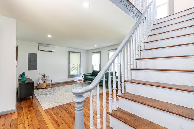 staircase with hardwood / wood-style floors, a wall mounted air conditioner, and electric panel