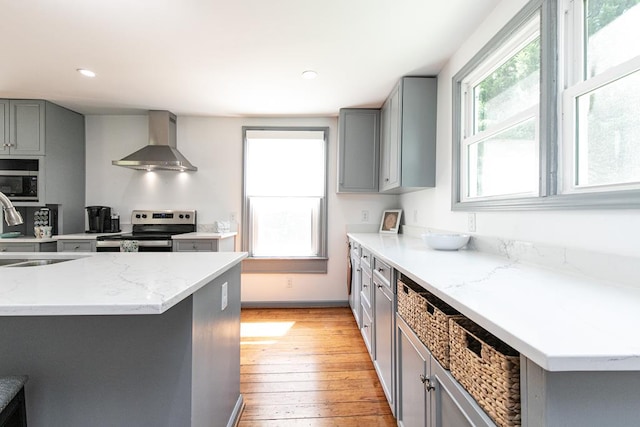 kitchen with sink, gray cabinetry, light wood-type flooring, stainless steel appliances, and wall chimney range hood