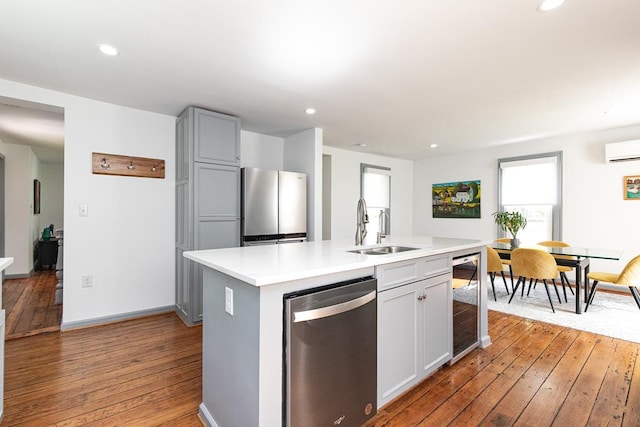 kitchen with sink, stainless steel appliances, light hardwood / wood-style floors, an island with sink, and beverage cooler