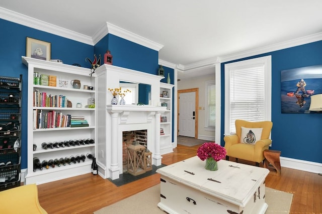 living room featuring a fireplace with flush hearth, wood finished floors, baseboards, and ornamental molding