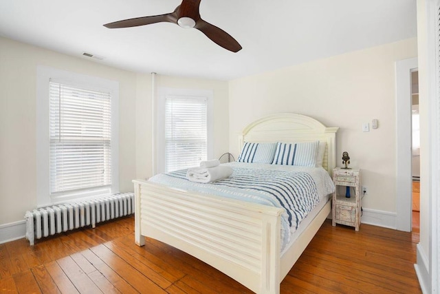 bedroom featuring visible vents, baseboards, ceiling fan, radiator heating unit, and wood-type flooring