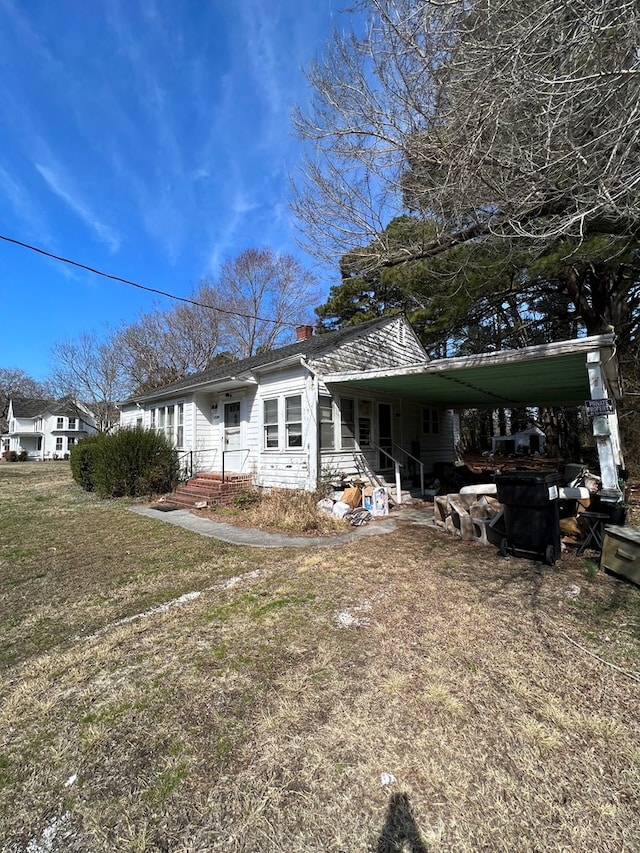 rear view of house featuring an attached carport, a yard, and a chimney