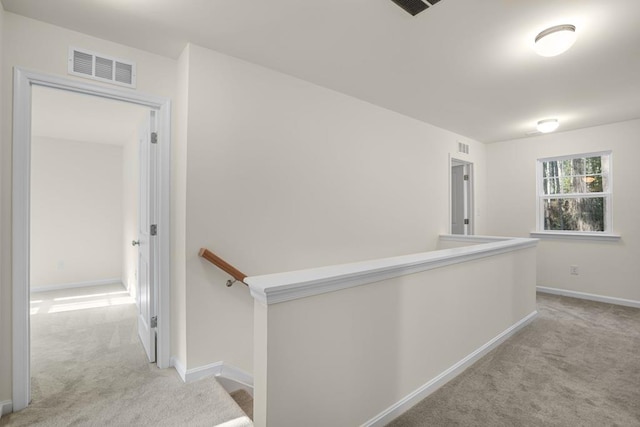 hallway featuring carpet, visible vents, baseboards, and an upstairs landing