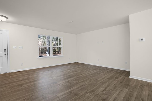 empty room with dark wood-style floors, visible vents, and baseboards