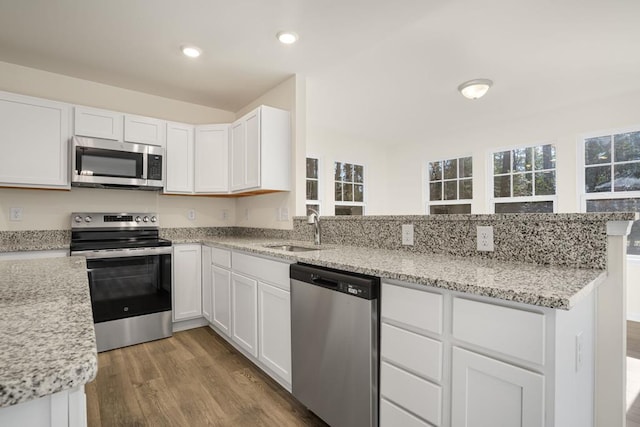 kitchen with a peninsula, wood finished floors, a sink, white cabinetry, and appliances with stainless steel finishes