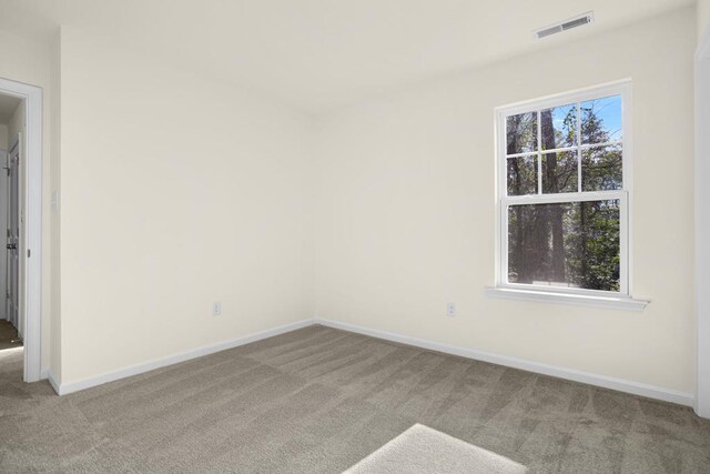 carpeted empty room featuring a healthy amount of sunlight, baseboards, and visible vents