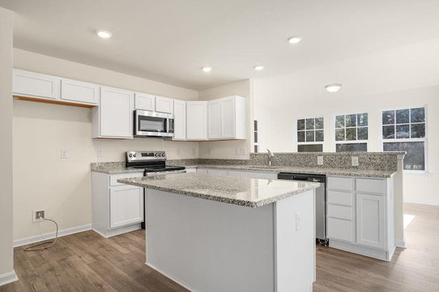 kitchen featuring a peninsula, white cabinetry, stainless steel appliances, and wood finished floors