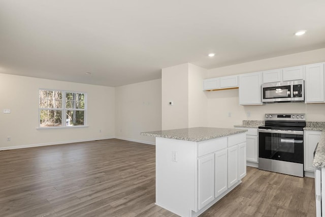 kitchen with light stone counters, a center island, stainless steel appliances, light wood-type flooring, and white cabinetry