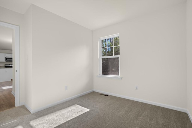 spare room with carpet flooring, visible vents, and baseboards