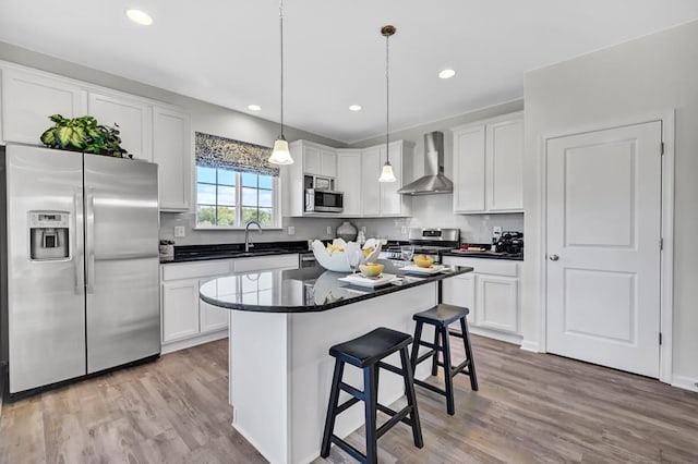 kitchen featuring a center island, white cabinets, hanging light fixtures, wall chimney exhaust hood, and appliances with stainless steel finishes