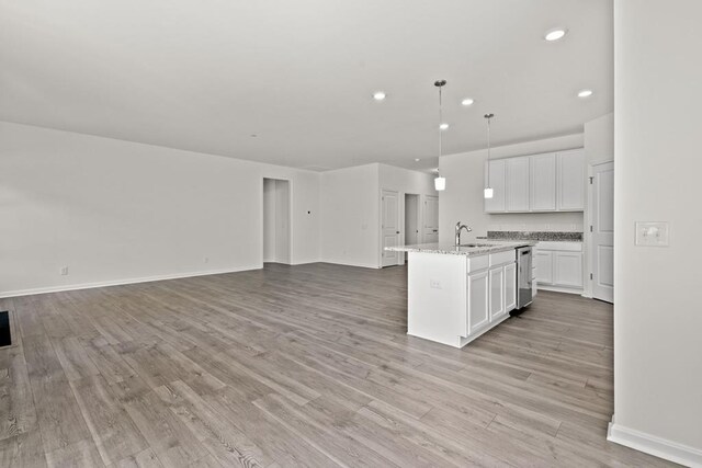 kitchen featuring a center island with sink, white cabinets, sink, light stone countertops, and decorative light fixtures