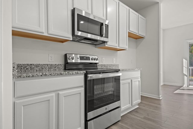 kitchen featuring white cabinets, light wood-type flooring, stainless steel appliances, and light stone counters